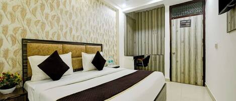 Habitación de hotel con cama, mesita de noche, planta en maceta y vista al exterior.