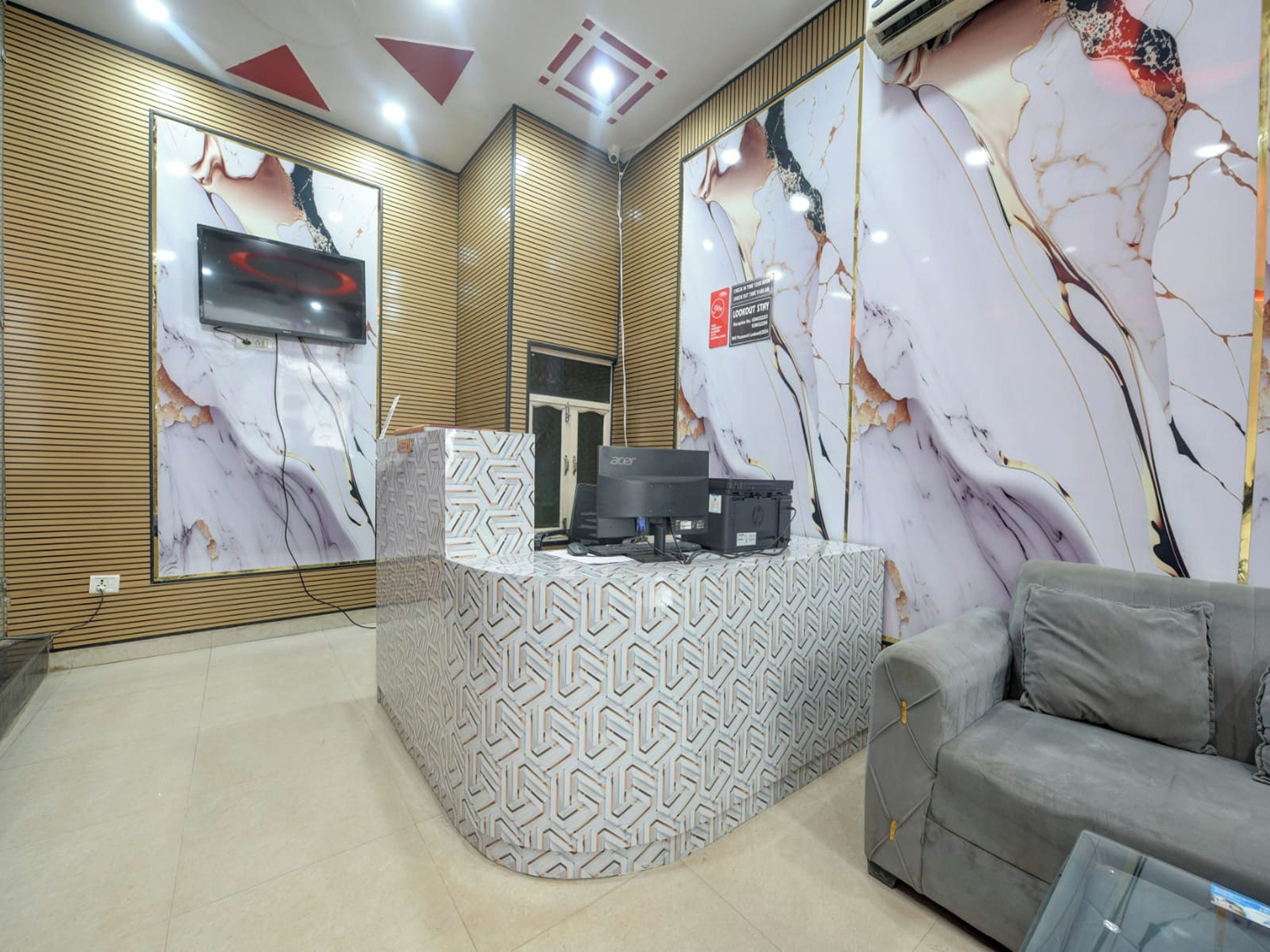 A reception area with a marble-patterned wall, a grey sofa, and a reception desk with a patterned cover.