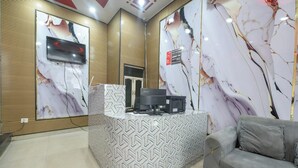 A reception area with a marble-patterned wall, a grey sofa, and a reception desk with a patterned cover. - Hotel Lookout Stay (New Delhi)