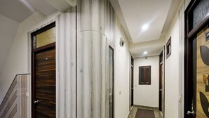 Un couloir avec des portes en bois, un sol carrelé de marbre et un escalier sur la gauche.