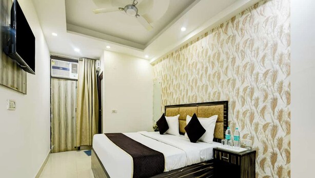 A hotel room with a bed, a nightstand, a TV, and a ceiling fan. - Hotel Lookout Stay (New Delhi)