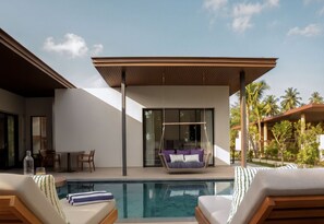 A modern outdoor pool area with a hanging chair, lounge chairs, and a glass-enclosed patio. - Chatrium Phuket Rawai  (Rawai)