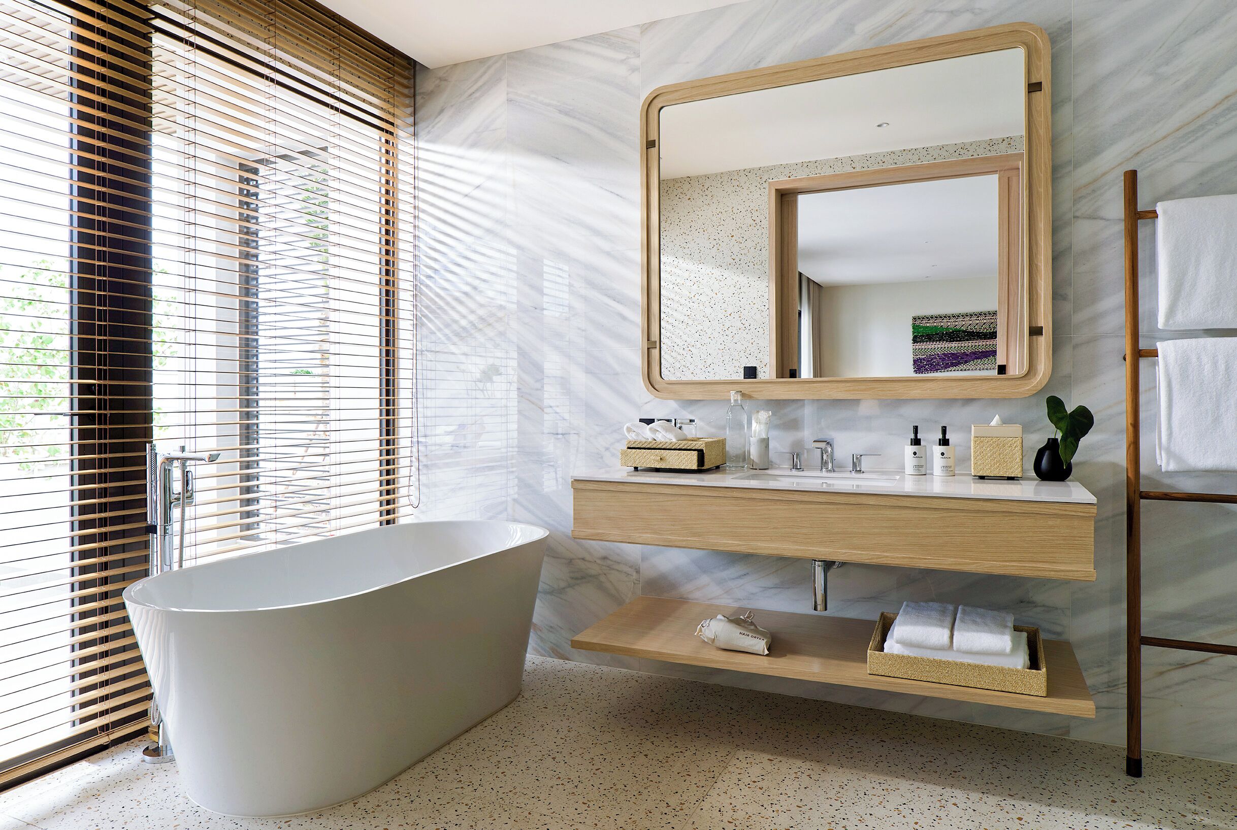 A modern bathroom with a freestanding bathtub, a wooden vanity with a mirror, and a towel rack.