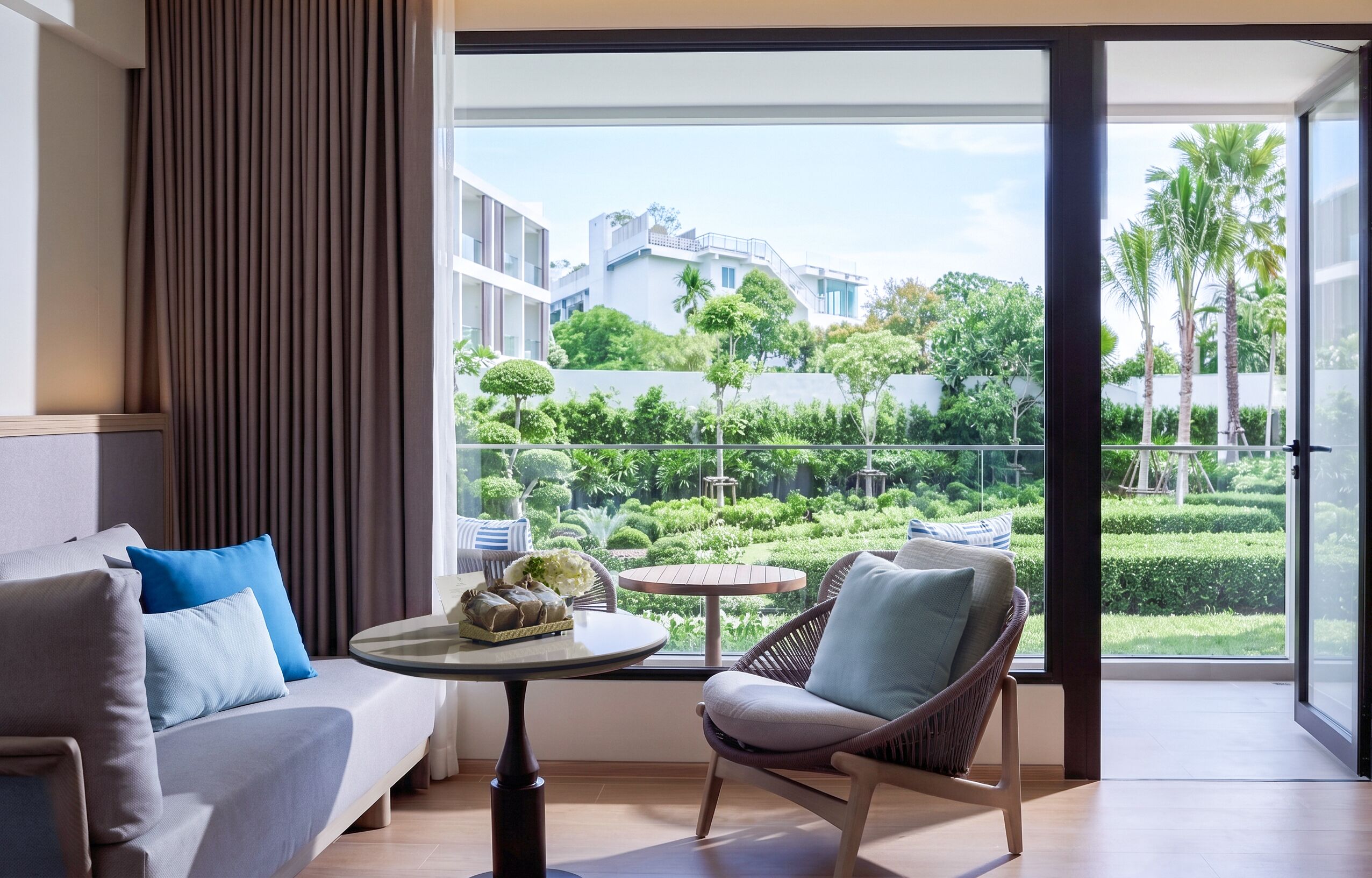 A modern hotel room with a balcony, a sofa, a chair, and a small table with a decorative item.