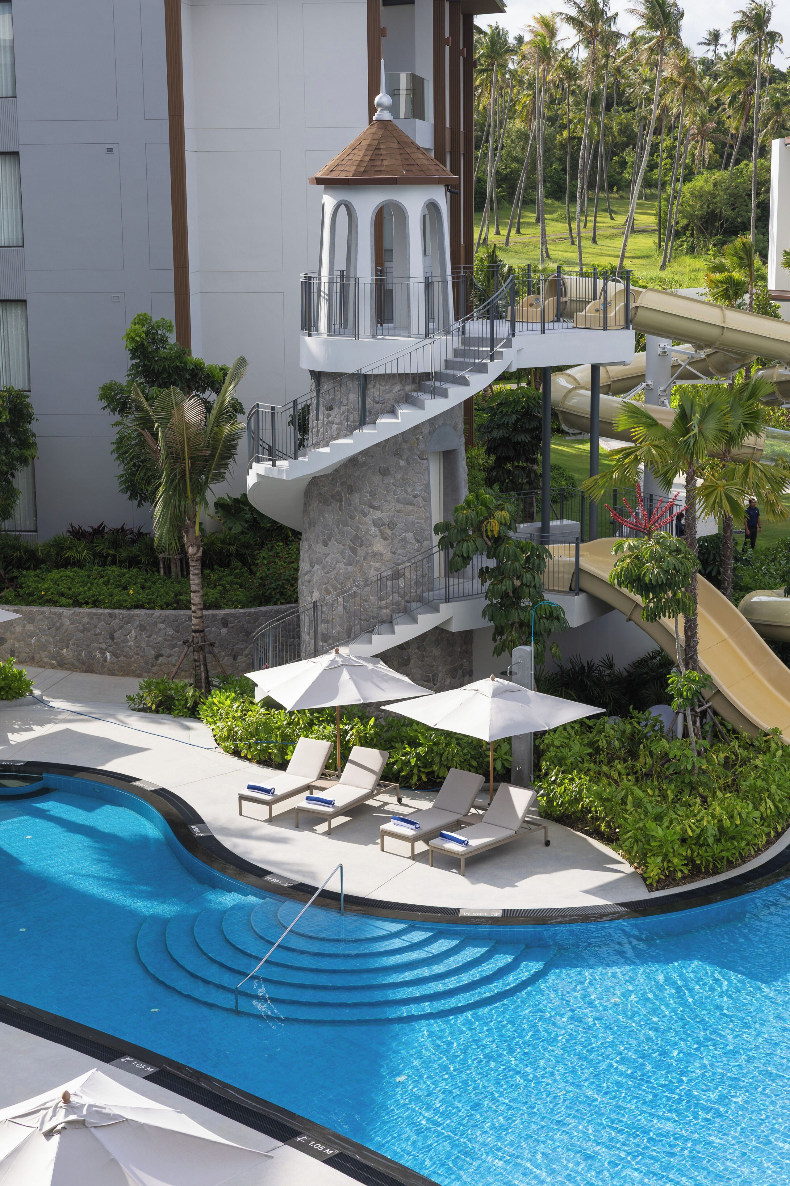 A swimming pool with lounge chairs and umbrellas, a stone tower, and a slide.