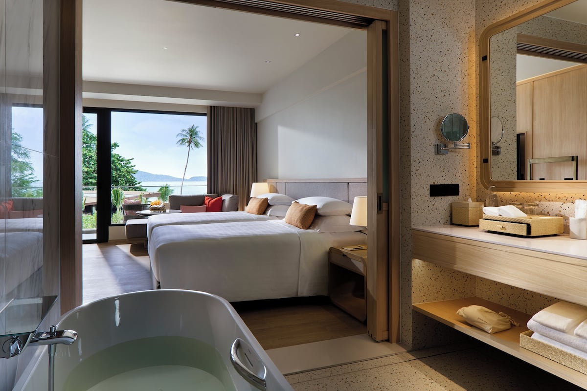 A hotel room with a large bed, a bathtub, a bathroom with a mirror, and a view of the outdoors.