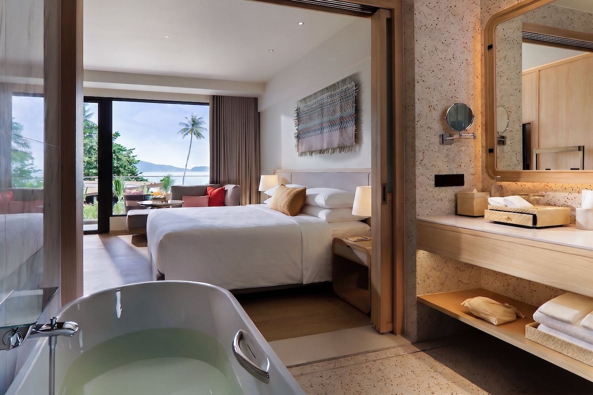 A hotel room with a large bed, a bathtub, a sitting area with a view, and a bathroom with a mirror and towel rack.