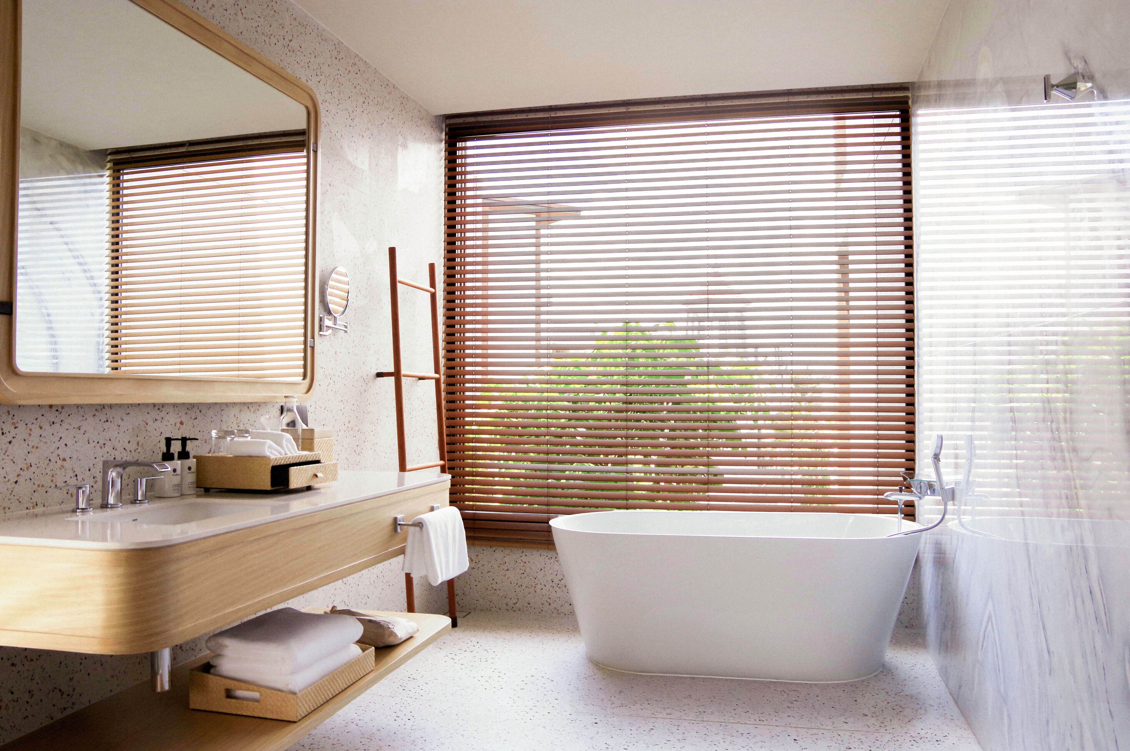 Un baño moderno con una bañera independiente, un tocador con espejo y una ventana con persianas.