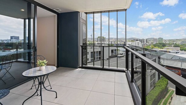 A balcony with a glass table and chairs, a potted plant, and a city view.