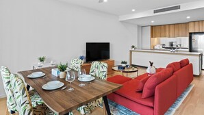 A modern apartment with a dining area, a living room with red sofas, a kitchen, and a ceiling fan.