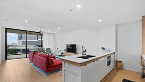 A modern apartment with a kitchen island, a red sofa, and a dining area with a city view.