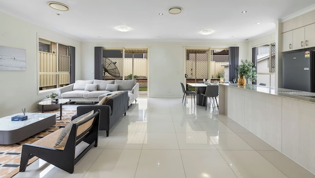A modern living room with a sofa, coffee table, and dining area with chairs. - Spacious 4BR Family Home in Inala | Quiet Street (Inala)