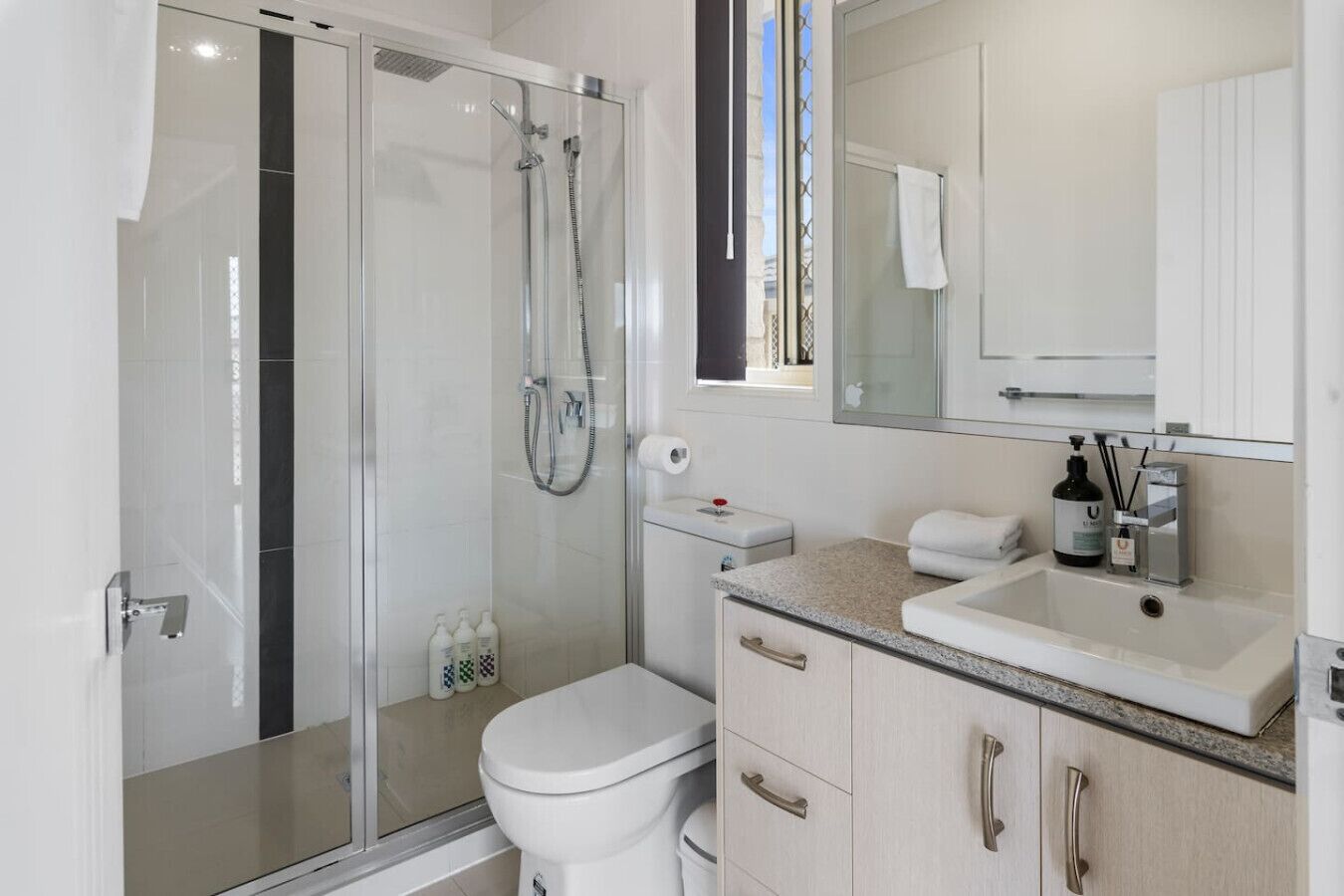 Une salle de bain moderne avec une douche à l’italienne en verre, des toilettes, un lavabo avec un meuble-vasque et un miroir au-dessus du lavabo.