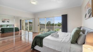 A bedroom with a large bed, a mirror, and a view through a sliding glass door. - Spacious 4BR Family Home in Inala | Quiet Street (Inala)