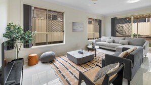 A modern living room with a grey sofa, a coffee table, and a potted plant. - Spacious 4BR Family Home in Inala | Quiet Street (Inala)
