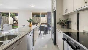 A modern kitchen with a central island, stainless steel appliances, and a dining area with a view of the backyard. - Spacious 4BR Family Home in Inala | Quiet Street (Inala)