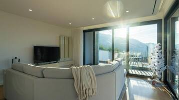 Una sala de estar moderna con un sofá modular grande, un televisor de pantalla plana y un balcón con vistas a las montañas.