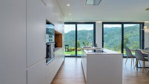 A modern kitchen with a central island, large windows, and a view of a mountainous landscape. - Gerês Paradise (Vieira do Minho)