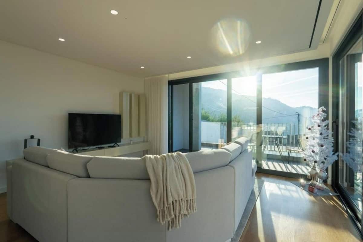A modern living room with a large sectional sofa, a flat-screen TV, and a balcony with a view of the mountains.