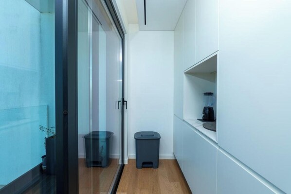 A modern kitchen with white cabinets, a glass door, and a small trash bin. - Gerês Paradise (Vieira do Minho)