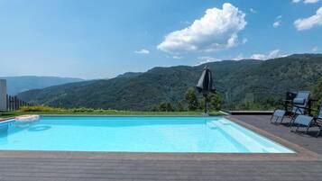 A swimming pool with a view of mountains, surrounded by lounge chairs and an umbrella.