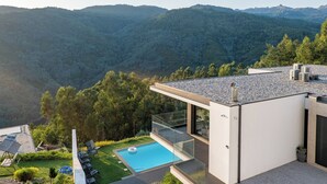 Uma casa moderna com piscina no terraço, rodeada por vegetação exuberante e montanhas.