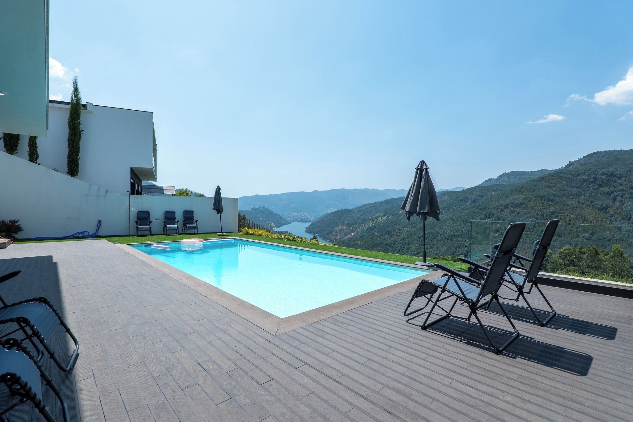 A swimming pool with a view of a valley, surrounded by a deck with lounge chairs and umbrellas.