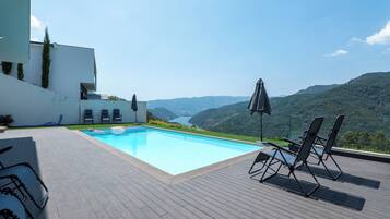 A swimming pool with a view of a valley, surrounded by a deck with lounge chairs and umbrellas.