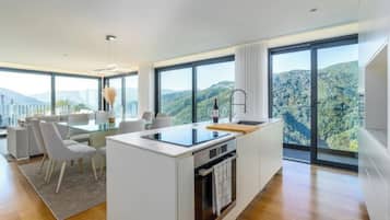 A modern kitchen with a central island, large windows, and a dining area with white furniture.