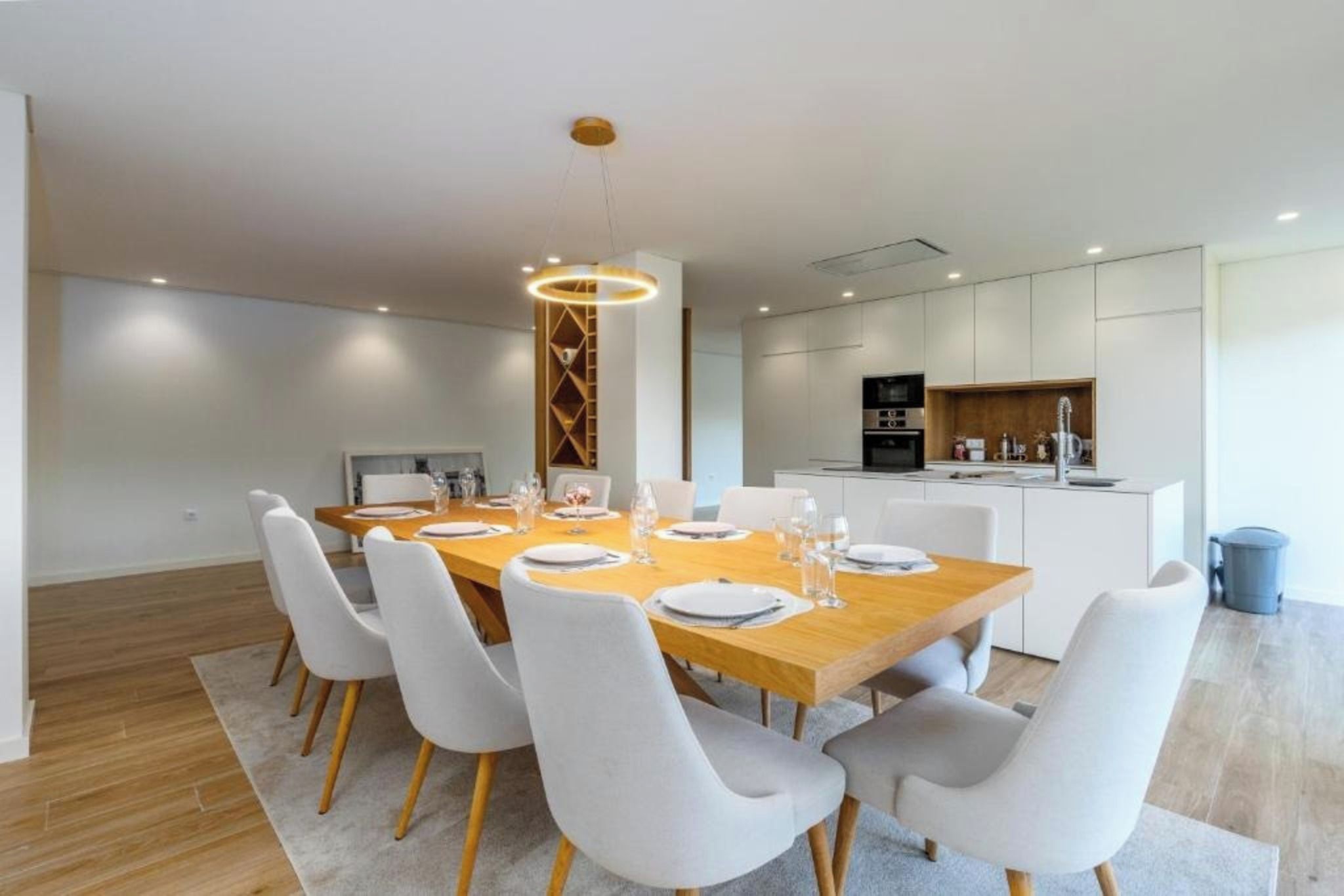 A modern dining area with a wooden table set for six, surrounded by white chairs.
