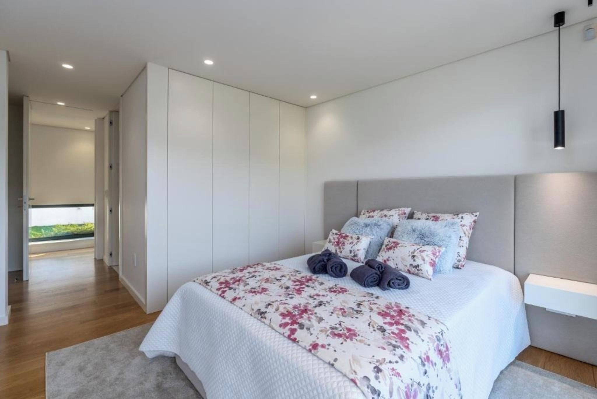 Un dormitorio moderno con una cama grande, paredes blancas y vistas al exterior.