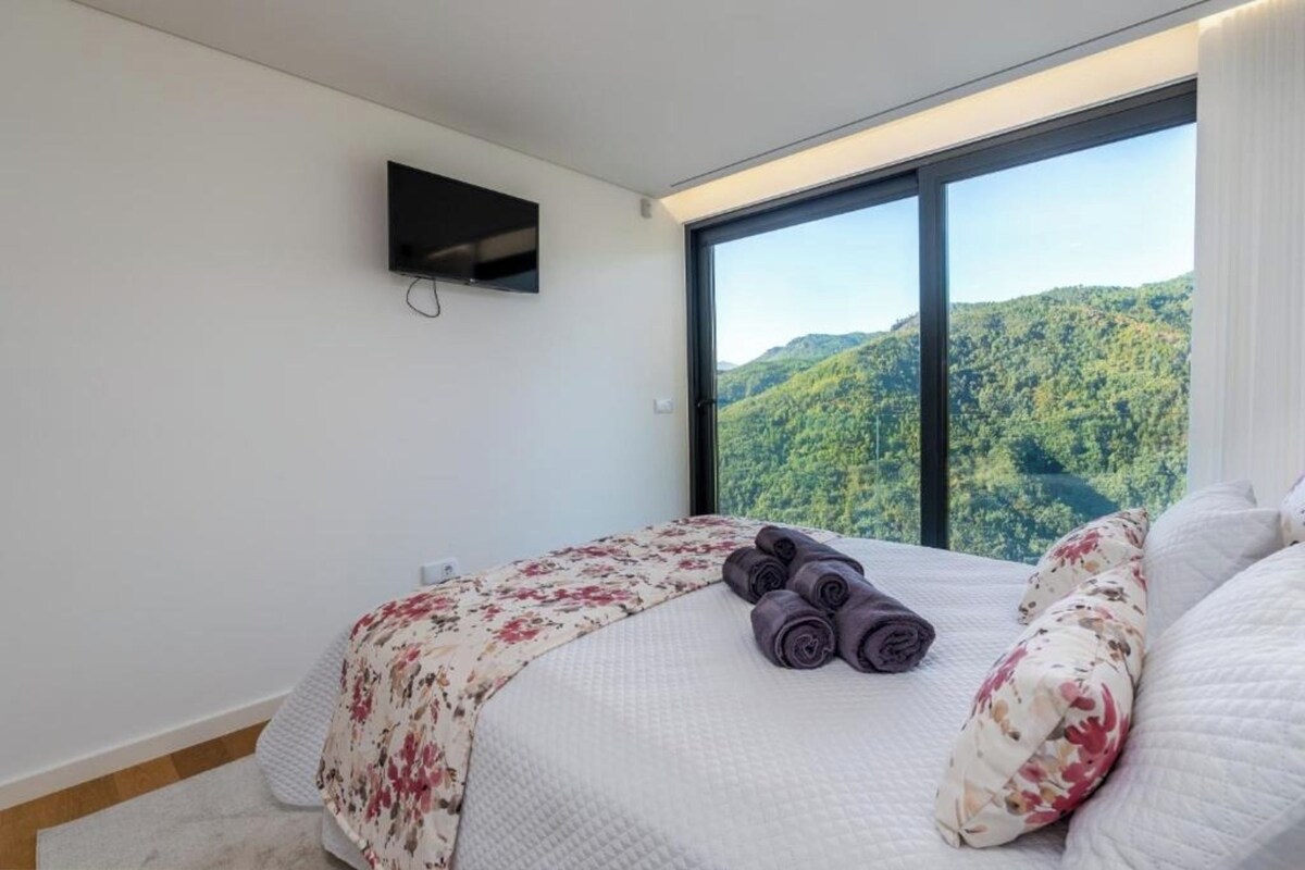 A bedroom with a large window, a bed with a floral bedspread, and a rolled towel on the bed.