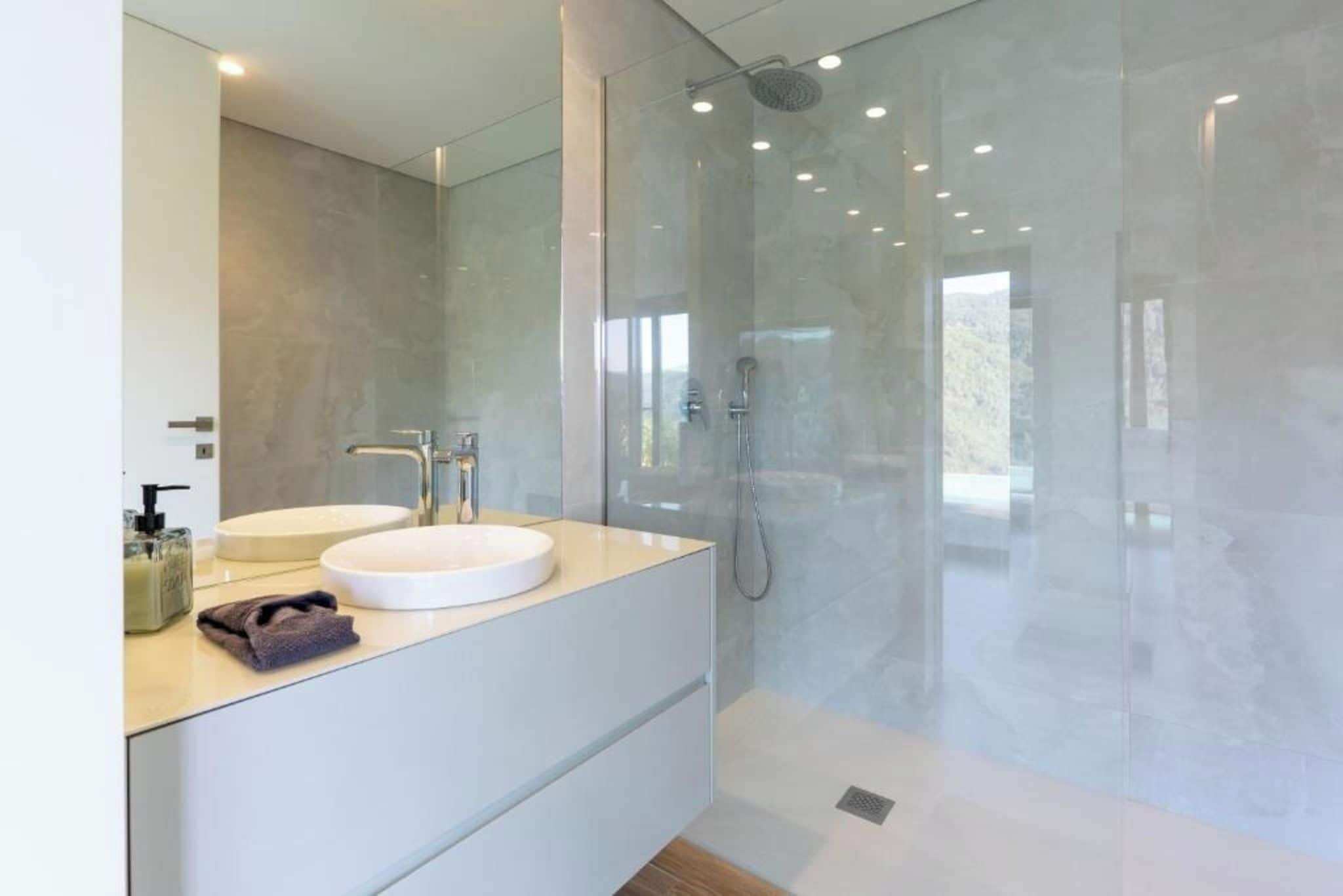 A modern bathroom with a glass-enclosed shower, a white vanity with a round sink, and a large mirror.
