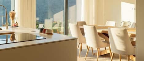 A modern dining area with a large table and chairs, a kitchen island with a sink, and a view of the outdoors.