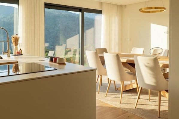 A modern dining area with a large table and chairs, a kitchen island with a sink, and a view of the outdoors. - Gerês Paradise (Vieira do Minho)