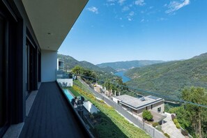 Un bâtiment moderne doté d’un balcon donnant sur un paysage montagneux et un lac.