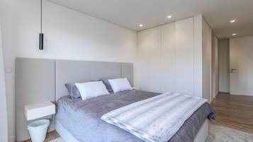 A modern bedroom with a large bed, a bedside table, a trash bin, and a hanging light fixture.