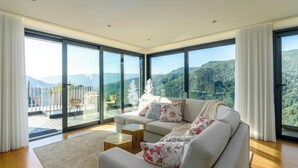 A modern living room with a large sofa, a coffee table, and a view of a mountainous landscape through floor-to-ceiling windows. - Gerês Paradise (Vieira do Minho)