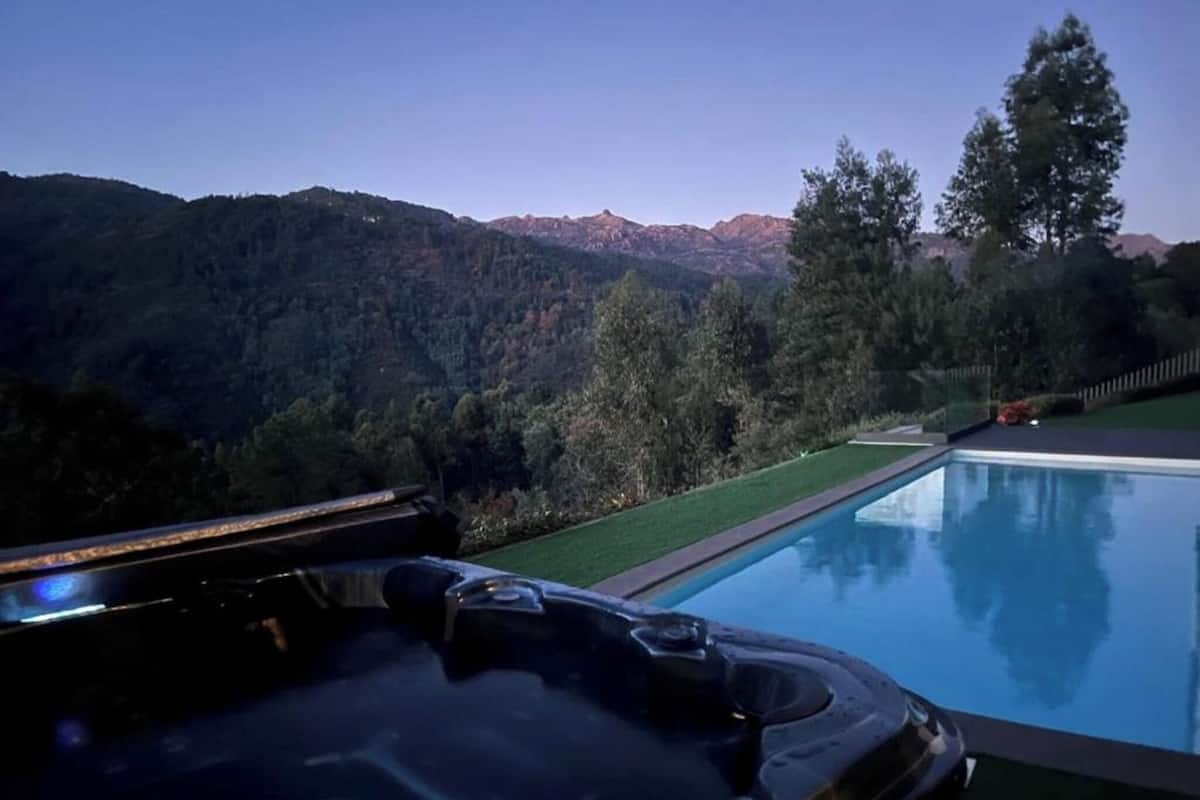 A hot tub with a mountain view, surrounded by a well-maintained lawn and trees.