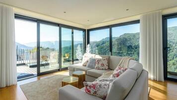 Una sala de estar moderna con un sofá grande, una mesa de centro y vistas a un paisaje montañoso a través de ventanales.