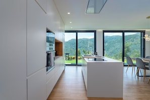 A modern kitchen with a central island, large windows, and a view of a mountainous landscape. - Gerês Paradise (Vieira do Minho)