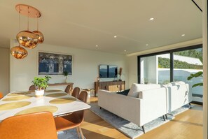 Un salon moderne avec un canapé blanc, une table à manger et des chaises, ainsi qu’une grande fenêtre donnant sur un paysage verdoyant.
