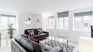 A modern living room with a black leather sofa, a glass coffee table, and a potted plant. - Walpole Court (London)