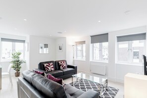 A modern living room with a black leather sofa, a glass coffee table, and a potted plant. - Walpole Court (London)