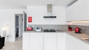 A modern kitchen with white cabinetry, a stainless steel range hood, and a countertop with a kettle and toaster. - Walpole Court (London)