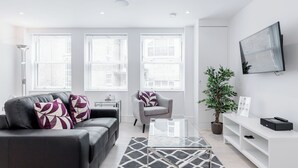 A modern living room with a grey sofa, a glass coffee table, and a white entertainment unit. - Walpole Court (London)
