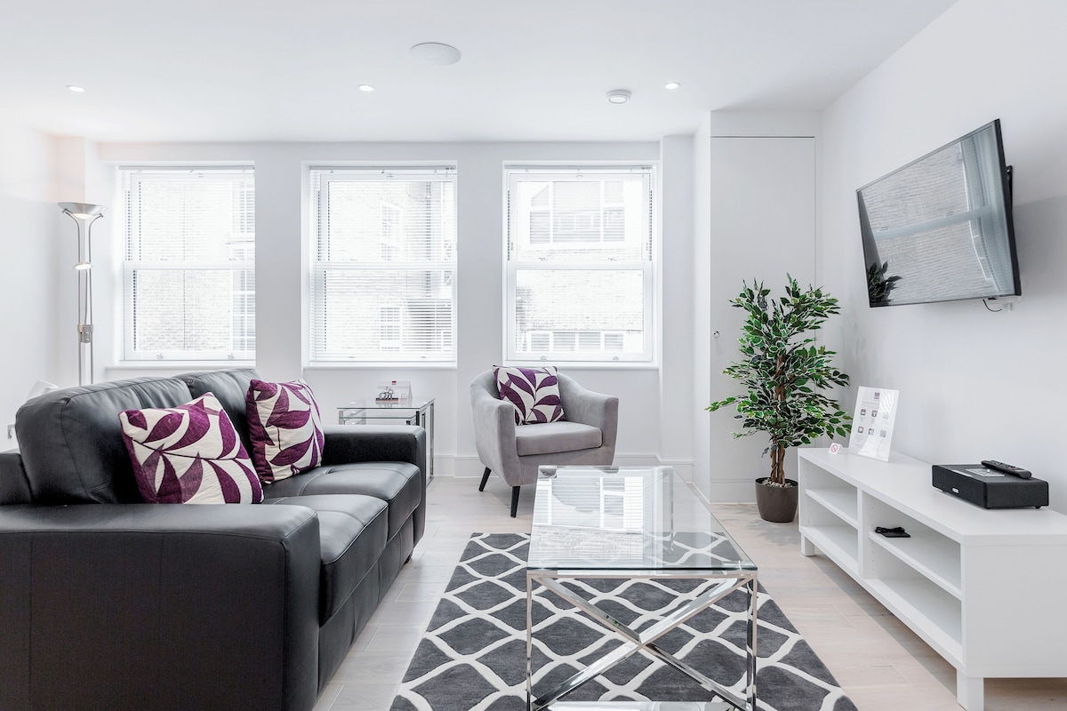 A modern living room with a grey sofa, a glass coffee table, and a white entertainment unit.