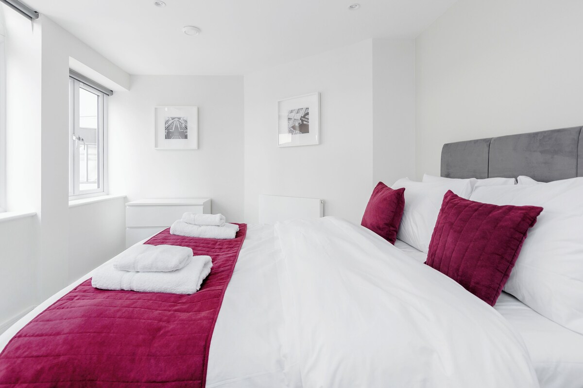 A hotel room with a large bed, white bedding, a grey headboard, and two framed pictures on the wall.