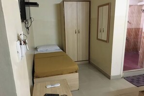 Ένα υπνοδωμάτιο με ένα κρεβάτι, μια ντουλάπα, ένα μικρό τραπέζι με ένα τηλεχειριστήριο και μια περιοχή με ντους.