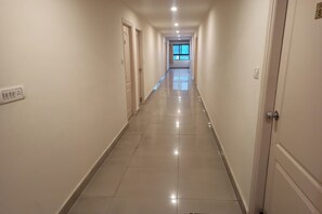Ένας μακρύς, στενός διάδρομος ξενοδοχείου με πόρτες και στις δύο πλευρές, πλακάκια στο δάπεδο και ένα παράθυρο στο  τέλος.